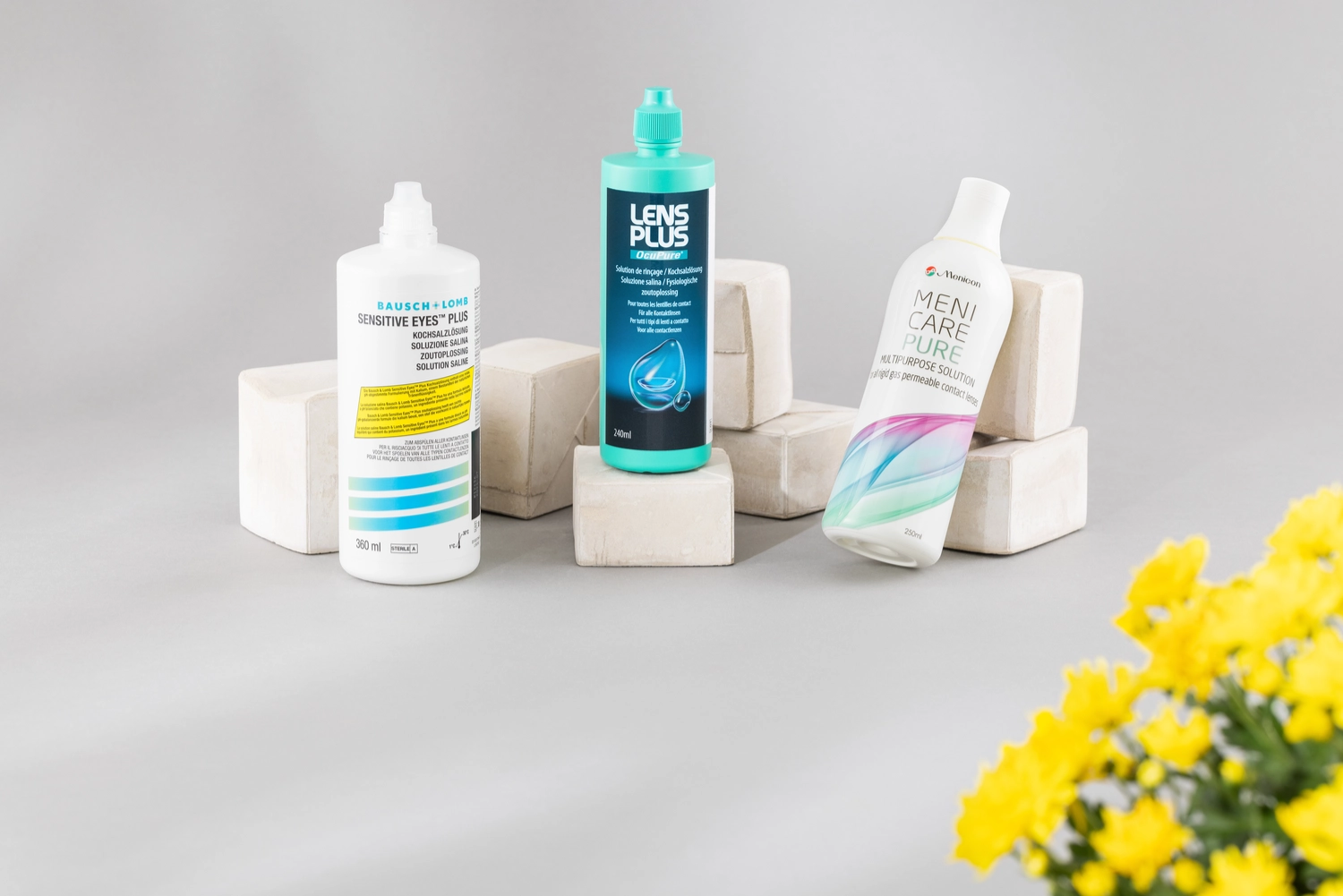 Pflegemittel kaufen Drei Pflegeprodukte arrangiert mit einer gelben Blume im Vordergrund.